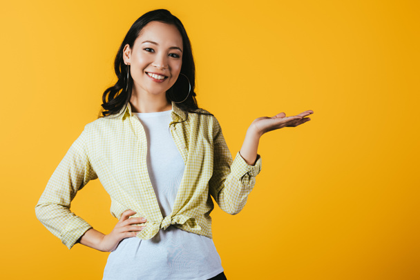 smiling asian girl presenting something isolated on yellow  - Фото, изображение