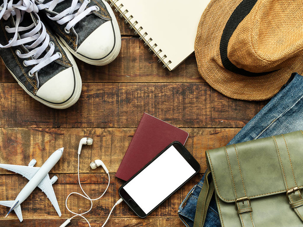 flat lay of passport , mobile , plane model , sneakers and traveler's accessories items on wooden background with copy space. travel and vacation concept - Foto, afbeelding