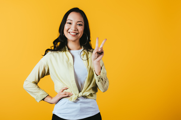 beautiful asian girl showing victory sign isolated on yellow - Foto, Imagem