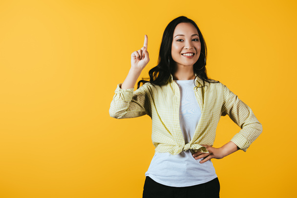 attractive happy asian girl pointing up isolated on yellow - Foto, Imagem