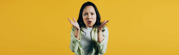 привлекательная сердитая азиатская женщина жестикулирует изолированно на желтом
 - Фото, изображение