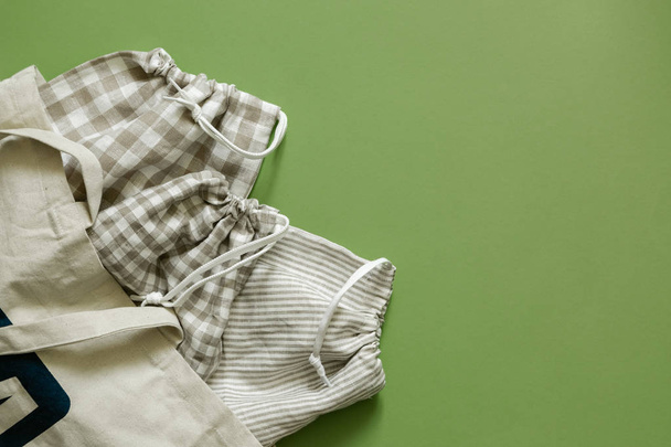 Zero waste concept - reusable cotton bags and glass jars on green background - Fotó, kép