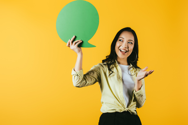 usmívající se asijská žena s bublinou řeči, izolovaná na žluté - Fotografie, Obrázek