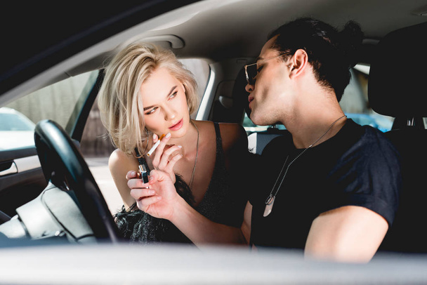 stylish handsome man lighting cigarette for beautiful girl in car - Фото, изображение
