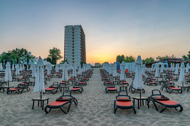 Krzesła i parasole na pięknej plaży o wschodzie słońca w Słonecznym Brzegu na wybrzeżu Morza Czarnego w Bułgarii. - Zdjęcie, obraz