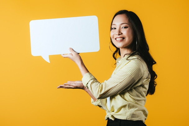 beautiful smiling asian girl presenting speech bubble, isolated on yellow  - Fotó, kép