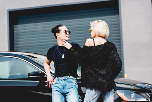 beautiful stylish couple posing near black car and garage - Фото, изображение