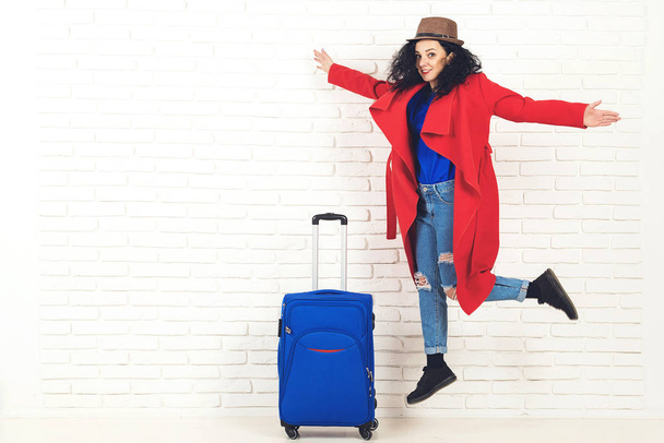 Γυναίκα ταξιδιώτη με βαλίτσα σε λευκό φόντο τούβλο. Ευτυχισμένο κορίτσι έτοιμο για ταξίδι. Έννοια ταξιδιών και τρόπου ζωής.  - Φωτογραφία, εικόνα
