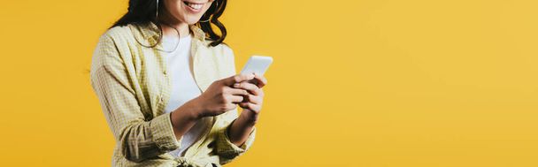 vista recortada de mujer joven usando teléfono inteligente aislado en amarillo
   - Foto, imagen
