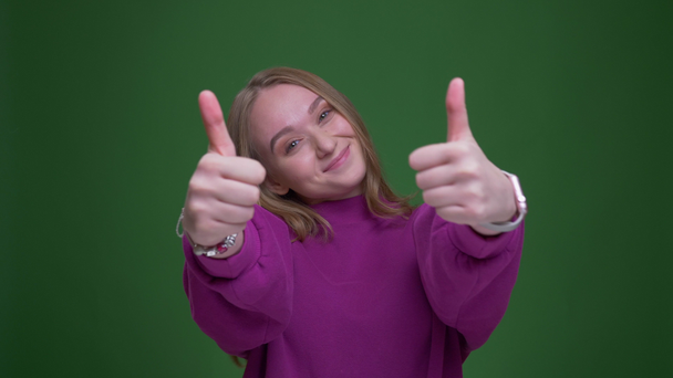 Pretty ginger female student makes thumbs-up gesture to show like and respect on green chroma background. - Footage, Video