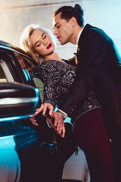 guapo elegante hombre y sensual joven mujer posando cerca de coche
 - Foto, Imagen