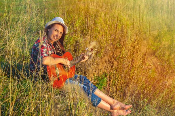 Beautiful, happy woman in the summer in the rays of the sunset with a guitar. Concept of creative freedom, fun and summer holidays - Photo, image