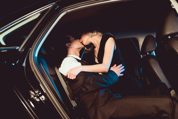 stylish man kissing sensual young woman in black car - Фото, зображення