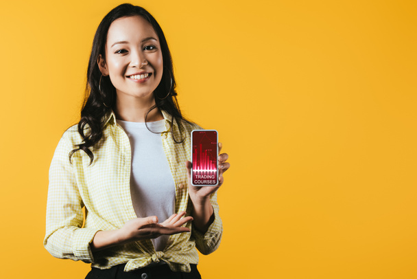 取引コースでスマートフォンを提示する幸せなアジアの女の子は、黄色で隔離 - 写真・画像