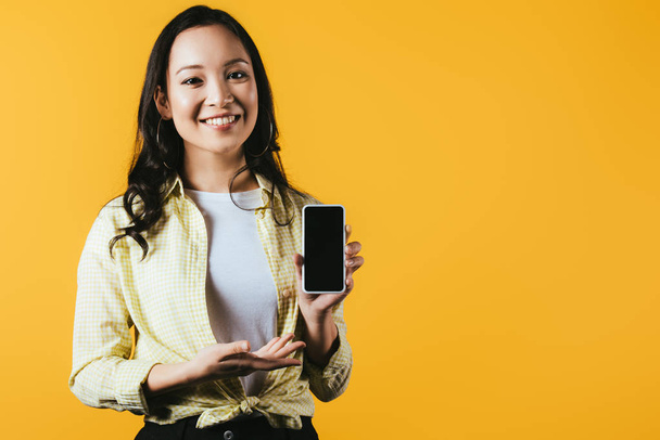 vonzó ázsiai lány bemutató okostelefon, üres képernyő elszigetelt sárga - Fotó, kép
