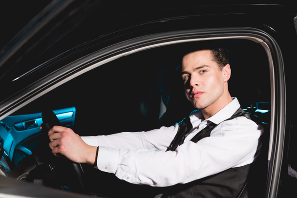 handsome stylish man in formal wear sitting in car and looking at camera - Foto, immagini