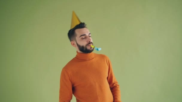 Playful young man wearing birthday hat blowing party horn having fun - Imágenes, Vídeo