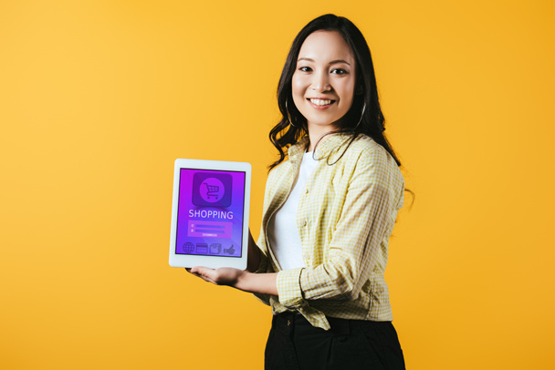 Gelukkig Aziatische meisje toont digitale tablet met winkelen app, geïsoleerd op geel - Foto, afbeelding