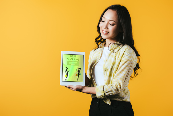 glückliches asiatisches Mädchen zeigt digitales Tablet mit bester Shopping-App, isoliert auf gelb - Foto, Bild