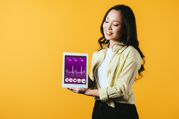 feliz asiático chica mostrando digital tableta con salud aplicación, aislado en amarillo
 - Foto, Imagen