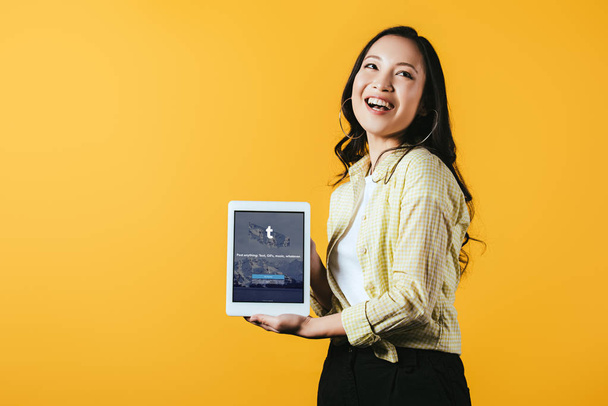 kyiv, ukraine - 16. April 2019: lächelndes asiatisches Mädchen zeigt digitales Tablet mit Tumblr-App, isoliert auf gelb - Foto, Bild