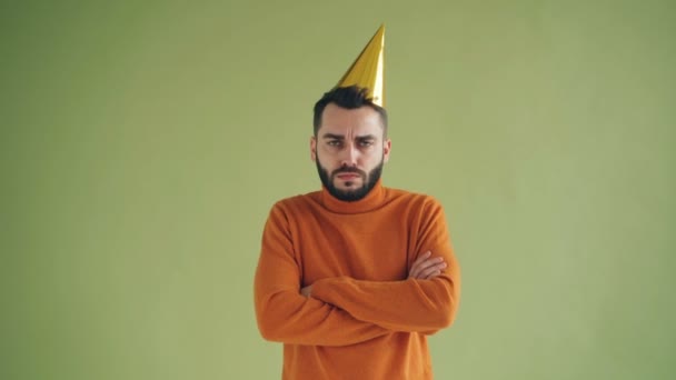 Portrait of upset man in party hat standing alone with arms crossed sighing - Кадры, видео