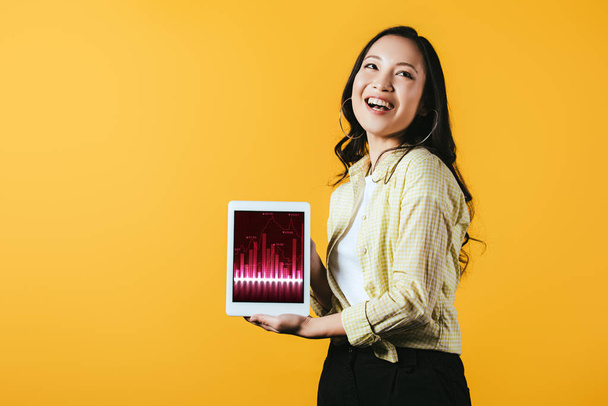 smiling asian girl showing digital tablet with graph, isolated on yellow - Foto, afbeelding