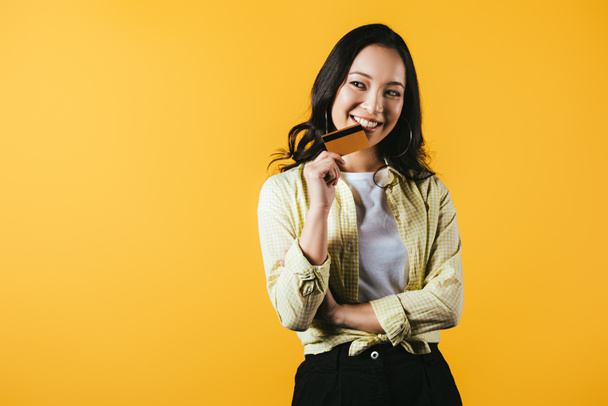 cheerful asian woman holding credit card, isolated on yellow - Fotografie, Obrázek