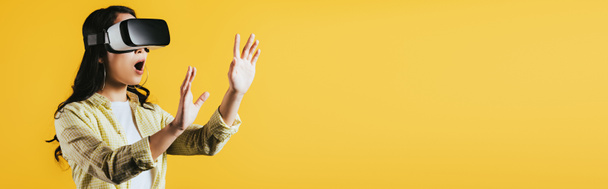 surprised woman gesturing and using Virtual reality headset, isolated on yellow  - Φωτογραφία, εικόνα