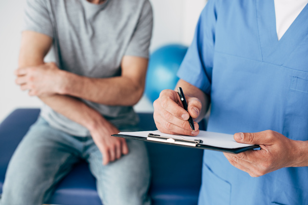 Обрезанный вид записи врачом на планшете и прикосновение пациента к руке в массажном кабинете в клинике
 - Фото, изображение