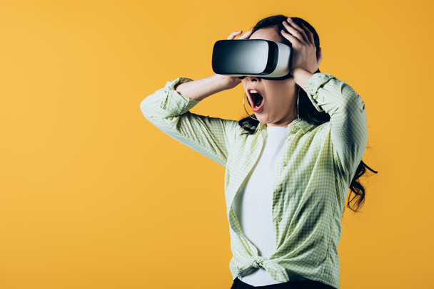 surprised yelling girl wearing Virtual reality headset, isolated on yellow - Fotoğraf, Görsel