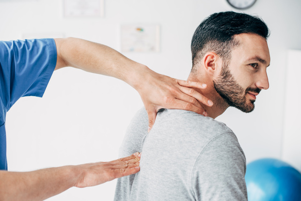 chiropractor massaging neck of good-looking man in hospital - Фото, зображення