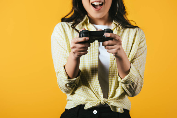KYIV, UKRAINE - APRIL 16, 2019: excited asian girl playing video game with joystick, isolated on yellow  - Фото, изображение