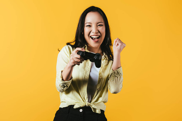 Kijów, Ukraina-16 kwietnia 2019: Happy Asian Girl gry wideo z joysticka, izolowane na żółtym  - Zdjęcie, obraz
