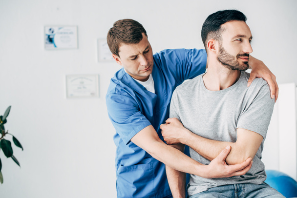 Physiotherapist massaging arm of handsome patient in hospital - Valokuva, kuva