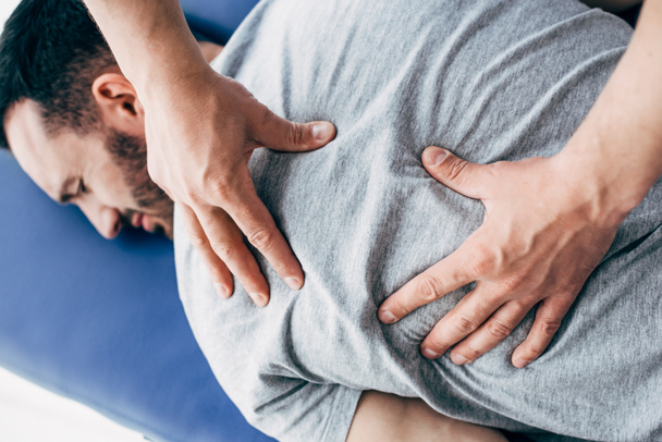Fysiotherapeut masseren rug van de mens liggend op massage tafel in het ziekenhuis - Foto, afbeelding