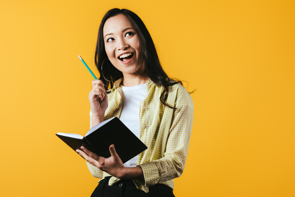 smiling asian girl with notebook and pen, isolated on yellow  - Photo, Image
