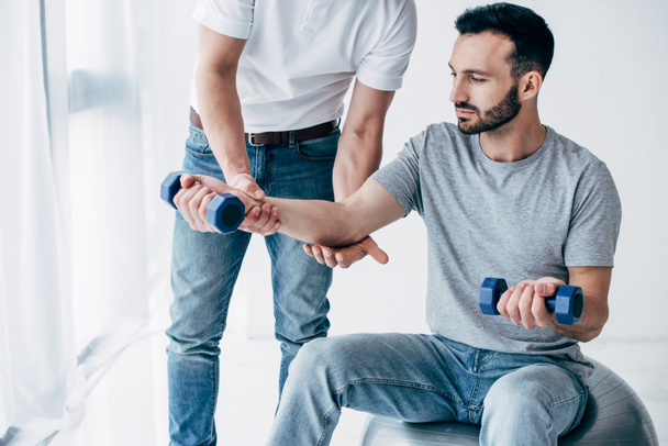 chiropractor stretching arm of handsome patient with dumbbells in hospital - Foto, Bild