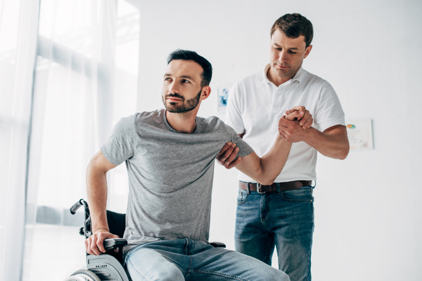 Fysiotherapeut helpen gehandicapte man in rolstoel tijdens herstel - Foto, afbeelding
