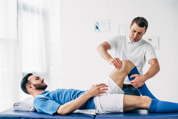 Fizjoterapeuta masowanie noga piłkarza leżącego na stole do masażu w szpitalu - Zdjęcie, obraz