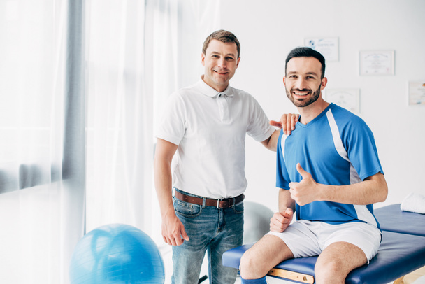 sorrindo Fisioterapeuta perto de jogador de futebol mostrando polegar no hospital
 - Foto, Imagem