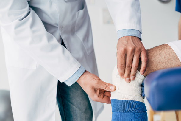 częściowy widok fizjoterapeuty oddanie bandaż elastyczny na nogę piłkarza - Zdjęcie, obraz