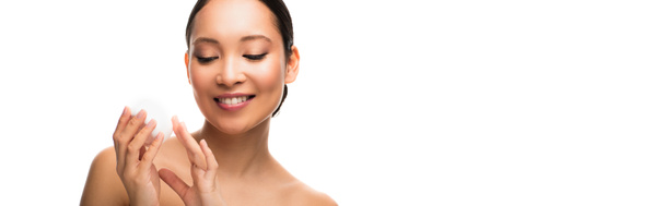 glimlachende Aziatische vrouw die gezichtscrème vasthoudt, geïsoleerd op wit - Foto, afbeelding