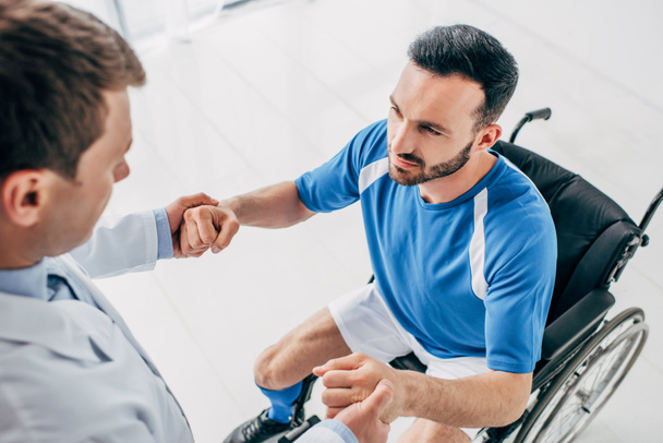 Fysioterapeutti auttaa vammaista jalkapalloilijaa pyörätuolissa toipumisen aikana
 - Valokuva, kuva