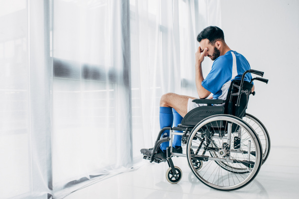 hombre molesto en uniforme de fútbol sentado en silla de ruedas en el hospital cerca de la ventana
 - Foto, Imagen