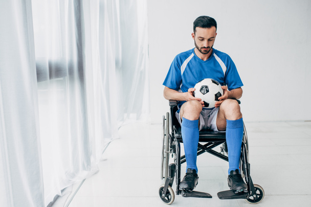 man in football uniform sitting in Wheelchair and holding soccer ball - Фото, зображення