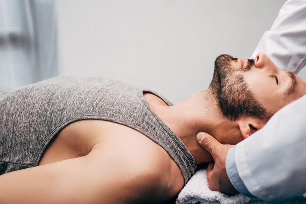 chiropractor massaging neck of man lying on towel in hospital - Photo, Image