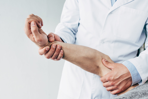 обрізаний вид хіропрактика розтягування руки пацієнта на сірому
 - Фото, зображення