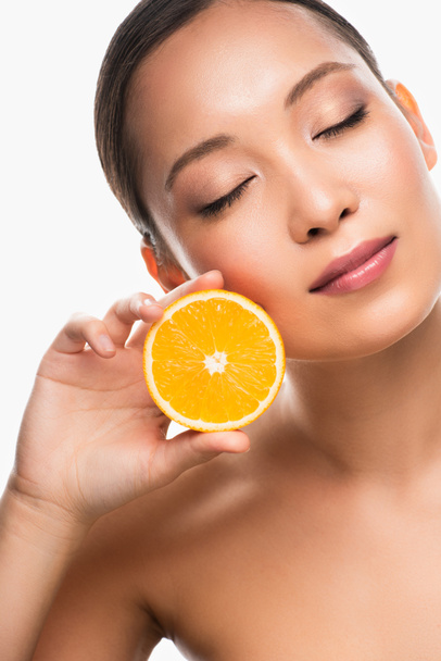 hermosa mujer asiática tierna con los ojos cerrados sosteniendo naranja, aislado en blanco
 - Foto, Imagen