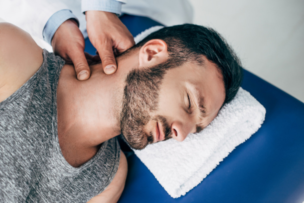 chiropraktik masíroval krk hezkého muže ležícího na masážním stole - Fotografie, Obrázek